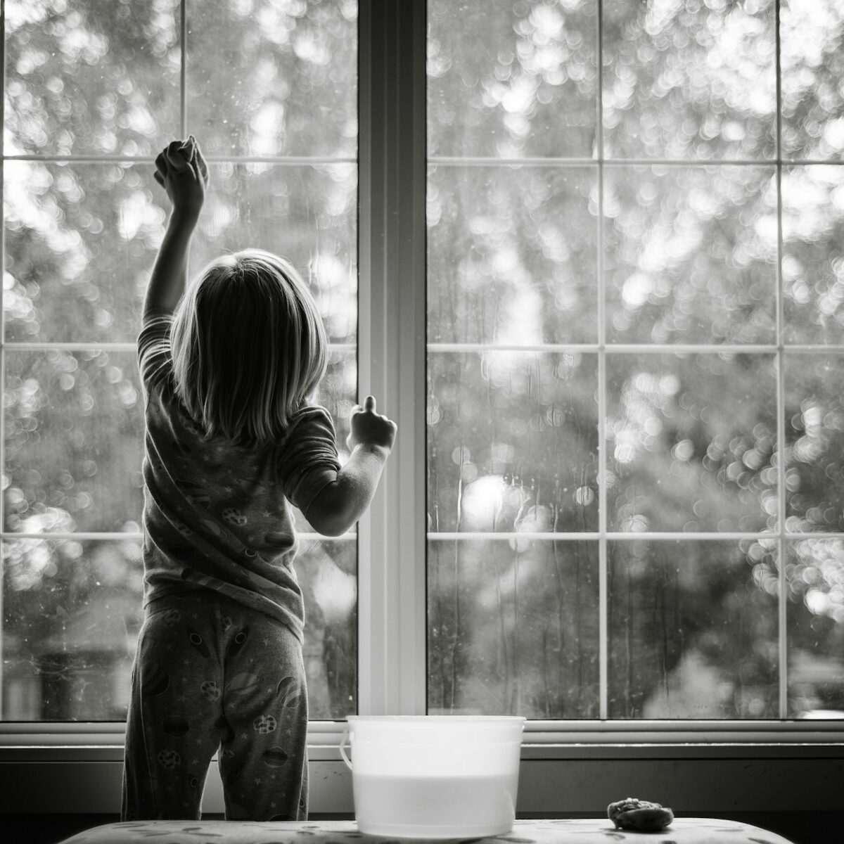 grayscale photo of girl in stripe shirt and pants standing by the window