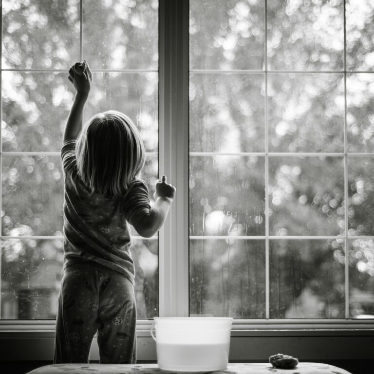 grayscale photo of girl in stripe shirt and pants standing by the window